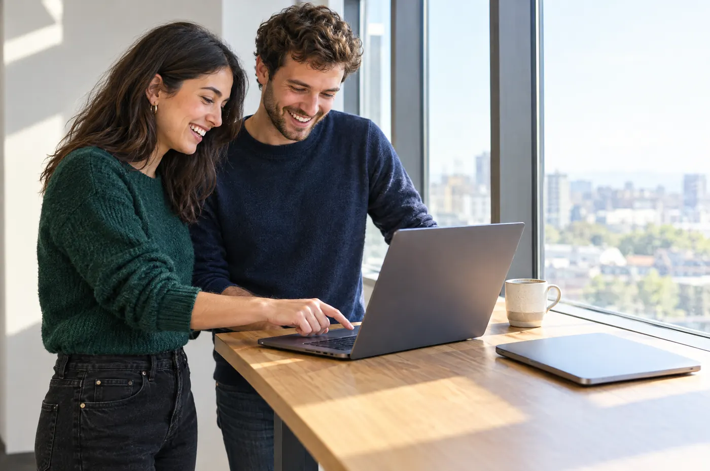 Two engineers at a standing desk sharing a laptop, smiling.